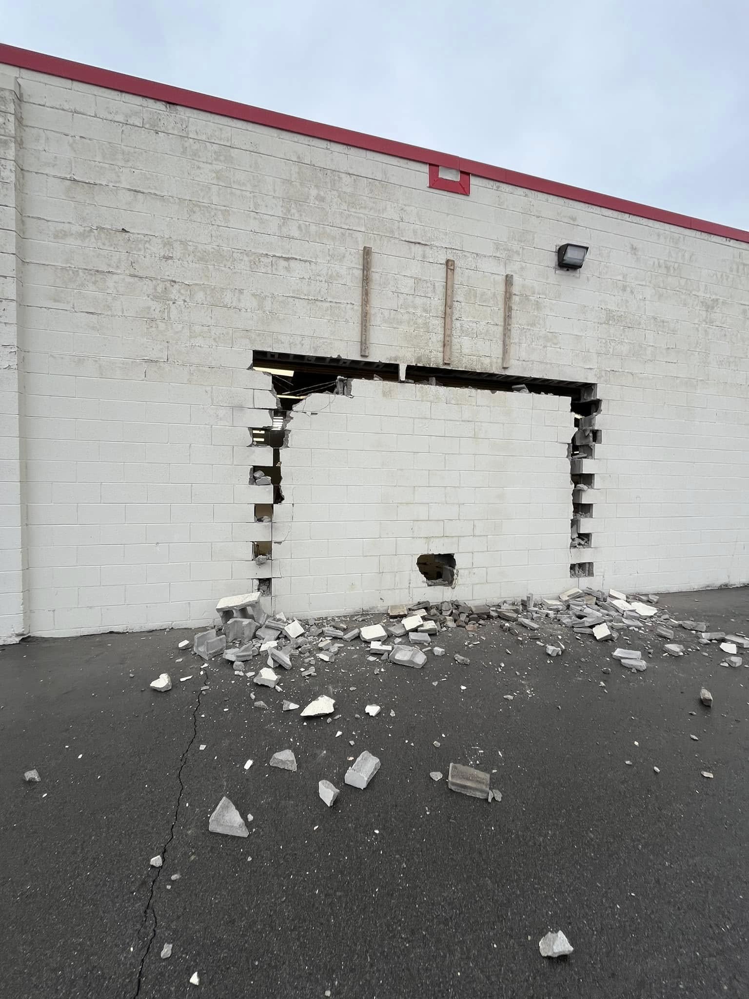 White brick exterior wall with a large rectangular hole, debris and broken bricks scattered on the ground.